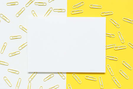 top view of blank white A4 paper with yellow and white paperclips spilled over a yellow and white paper background.の写真素材