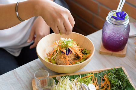 Woman mixing ingredients of Rice salad set on wood plate, Khao yam, Thai cuisineの写真素材