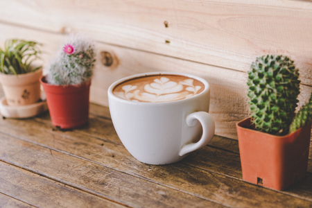 Latte art coffee cup with cactus pots on wooden table and wall, vintage styleの写真素材