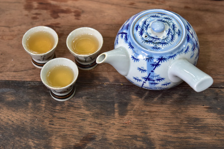 Hot tea pot with three ceramic cups on wooden table, top viewの写真素材