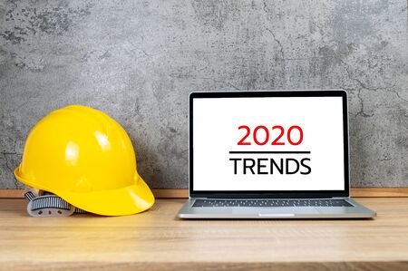 Yellow safety helmet and laptop computer with 2020 TRENDS text on white screenの写真素材