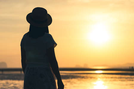 Back view of silhouette lonely woman standing  on beach at sunset timeの写真素材