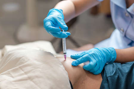 Doctor with hand gloves giving intramuscular injection with a conventional syringe needle on glutens muscle femaleの写真素材