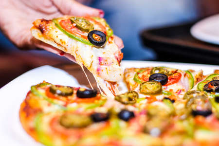 Slice of hot pizza large cheese with vegetables, tomato, onion and olives. Close Viewの写真素材