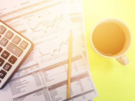 Business, finance or work day background concept : Top view of calculator, pencil, cup of coffee and company summary data charts on yellow backgroundの写真素材