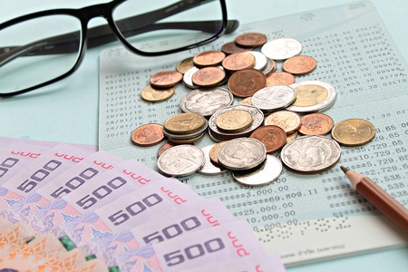 Business, finance or savings concept : Savings account passbook, Thai money baht, coins, glasses and pen on blue backgroundの写真素材