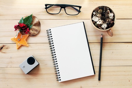 Business, work day, christmas or new year concept : Workspace desk with notebook, pencil, pine cones in tea wooden cup, eye glasses, christmas decoration and small action camera on wooden backgroundの写真素材
