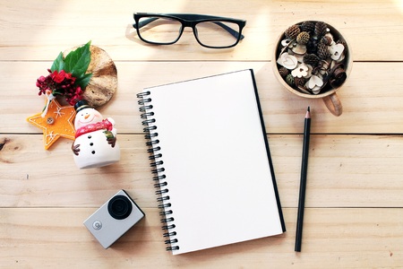 Business, work day, christmas or new year concept : Workspace desk with notebook, pencil, pine cones in tea wooden cup, eye glasses, christmas decoration and small action camera on wooden backgroundの写真素材