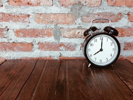 Retro black alarm clock with eight o'clock on wooden table and brick wall backgroundの写真素材