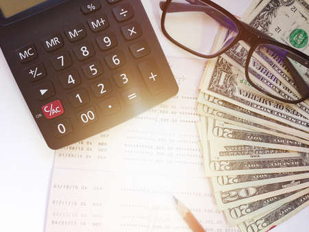 Business, finance, investment or accounting concept : Dollar money, calculator and saving account book or financial statement on office tableの写真素材