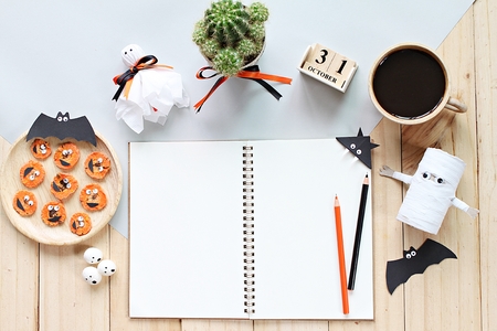 Halloween, celebration or holiday background concept : Mock up of open notebook, paper crafts, cube calendar, grilled carrots with scary face and coffee cup, Top view or flat lay with copy spaceの写真素材