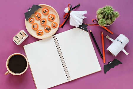 Halloween, celebration or holiday background concept : Mock up of open notebook, paper crafts, cube calendar, grilled carrots with scary face and coffee cup, Top view or flat lay with copy spaceの写真素材