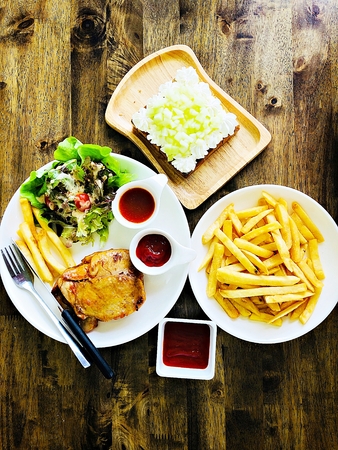 Food concept : Top view of grilled chicken steak, french fries or potato fries with ketchup and melon fruit toast on wooden tableの写真素材