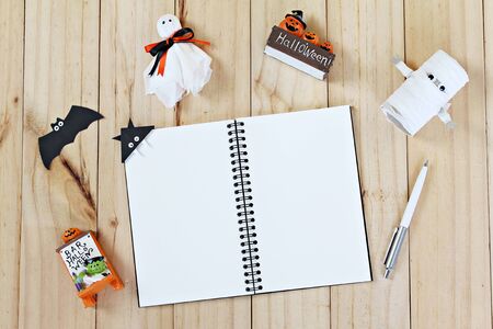 Halloween holiday background concept : Top view or flat lay of Notebook paper with Halloween decoration, ghosts and bat on wooden background with copy space, ready for adding or mock upの写真素材