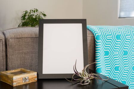Black 8x10 frame on a livingroom table top with a teal blanket airplant and puzzle box.