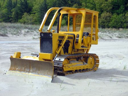 A three quarters profile of an abandoned yellow miniature bulldozer on a beach with sand in the...