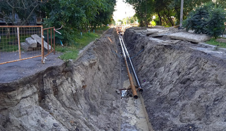 The road is dug up, pipes are in the pit, a pile of earth is nearby.の写真素材