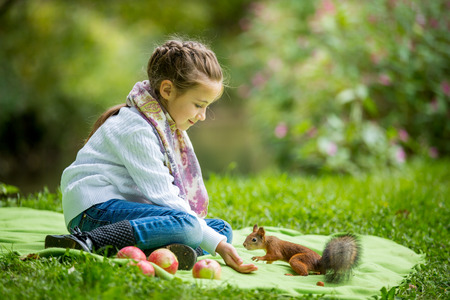 Little beautiful girl sitting on green lawn and feeding squirrel with nuts.の写真素材