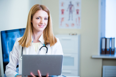 Portrait of friendly confident female doctor in hospital working on laptop. Enthusiastic medical staff at work. Female doctor in diagnostics room.の写真素材