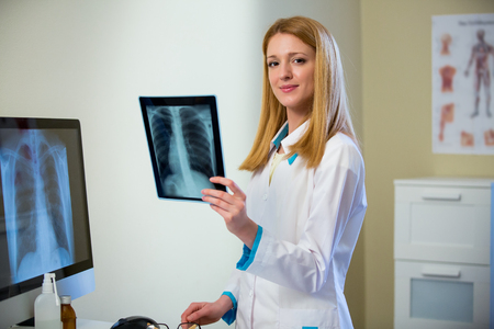 Portrait of friendly confident female doctor in hospital looking at x-ray. Enthusiastic medical staff at work. Female doctor in diagnostics room.の写真素材