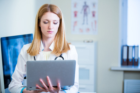 Portrait of friendly confident female doctor in hospital working on laptop. Enthusiastic medical staff at work. Female doctor in diagnostics room.の写真素材