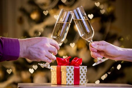 Two glasses of champagne and gift box with red bow. Background with blurred lights, bokeh of heart. Man and woman celebratingの写真素材