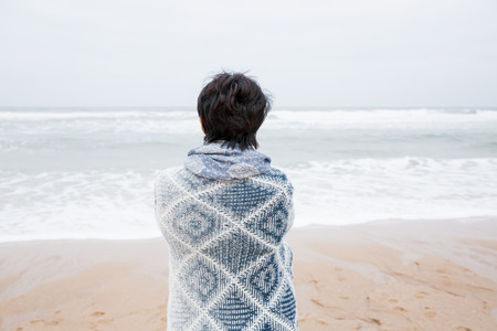 Single mature attractive woman standing on empty beach. Looking at the ocean. Rear view. Enjoying,...
