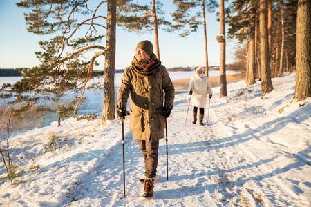 Winter sport in Finland - nordic walking. Man and Senior woman hiking in cold forest. Active people outdoors. Scenic peaceful Finnish landscape with snow.の写真素材
