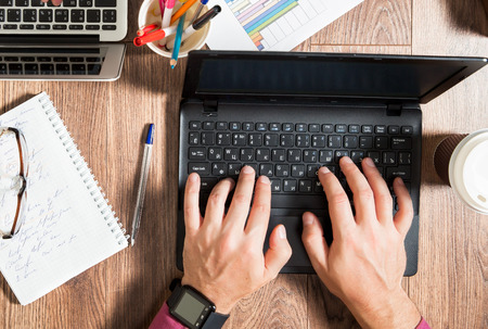 Business person working at office desk, typing and using laptop, top view. Smart watch on hand. Coffee cup, notepad and glasses around the workplace.の写真素材