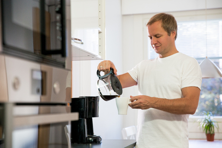Man in the kitchen pouring a mug of hot filtered coffee from a glass pot. Having breakfast in the morningの写真素材