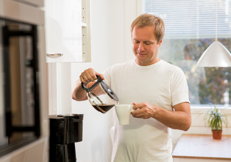 Man in the kitchen pouring a mug of hot filtered coffee from a glass pot. Having breakfast in the morningの写真素材
