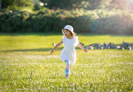 Adorable little girl, has happy fun with cheerful smiling face. Carefree child Running and jumping on green summer meadow, flying. Happiness, childhood and freedom concept.の写真素材