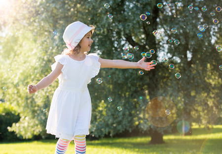 Adorable little girl, has happy fun with cheerful smiling face. Carefree child laughing, Running and jumping on green summer meadow, catching soap bubbles. Happiness, childhood and freedom concept.の写真素材