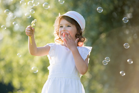 Adorable little girl, has happy fun with cheerful smiling face. Carefree child laughing, Running and jumping on green summer meadow, catching soap bubbles. Happiness, childhood and freedom concept.の写真素材