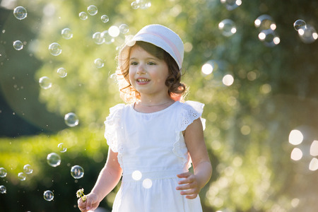 Adorable little girl, has happy fun with cheerful smiling face. Carefree child laughing, Running and jumping on green summer meadow, catching soap bubbles. Happiness, childhood and freedom concept.の写真素材
