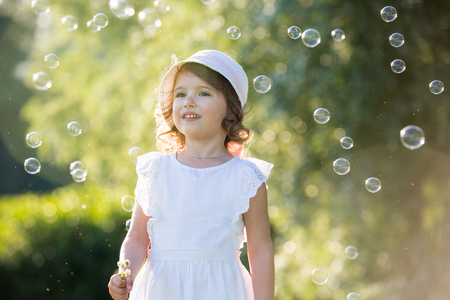 Adorable little girl, has happy fun with cheerful smiling face. Carefree child laughing, Running and jumping on green summer meadow, catching soap bubbles. Happiness, childhood and freedom concept.の写真素材