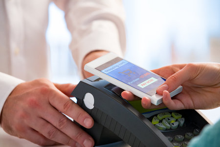 Wireless payment using smartphone and NFC technology. Close up. Customer paying with smart phone in pharmacy. Close Up shoppingの写真素材
