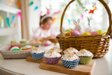Easter celebration, close-up table with glazed cupcakes, basket with Easter eggs and bunny. Happy family holidayの写真素材
