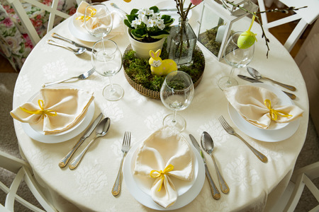 Beautiful served round table with decorations in dining room. Little yellow bunny, willow branches...