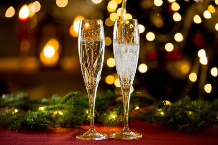 Background of two glasses of champagne, spruce branches on red table cloth. Living room decorated with lights and candles and Christmas treeの写真素材