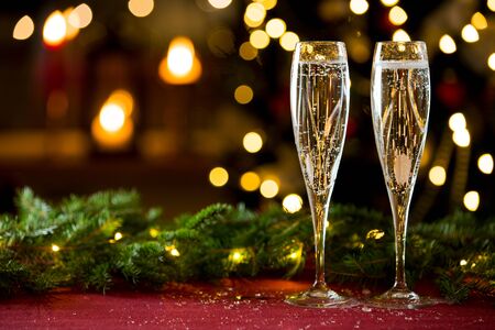 Background of two glasses of champagne, spruce branches on red table cloth. Living room decorated with lights and candles and Christmas treeの写真素材