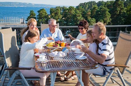 Big happy family having breakfast outdoors on terrace together, sitting around table, drinking...