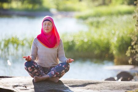 Attractive woman in hijab training in the park, meditating. Doing yoga exercises on fresh air and enjoying early morning. Healthy lifestyleの写真素材