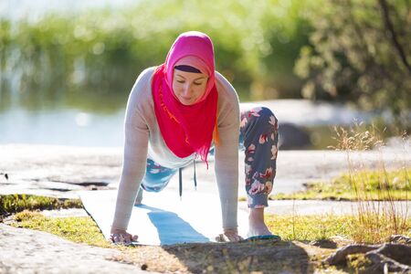 Attractive woman in hijab training in the park, meditating. Doing yoga exercises on fresh air and...