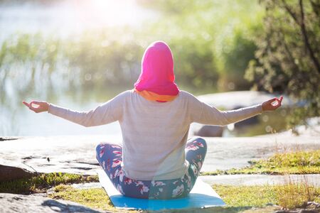 Attractive woman in hijab training in the park, meditating. Doing yoga exercises on fresh air and enjoying early morning. Healthy lifestyleの写真素材