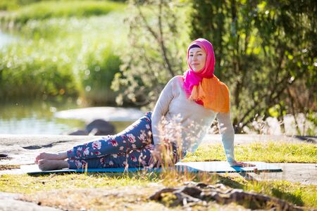 Attractive woman in hijab training in the park, meditating. Doing yoga exercises on fresh air and enjoying early morning. Healthy lifestyleの写真素材