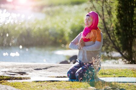 Attractive woman in hijab training in the park, meditating. Doing yoga exercises on fresh air and enjoying early morning. Healthy lifestyleの写真素材
