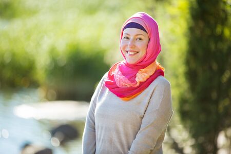 Attractive confident woman in hijab standing outdoors in sunny summer day, happily smiling. Muslim woman lifestyle conceptの写真素材