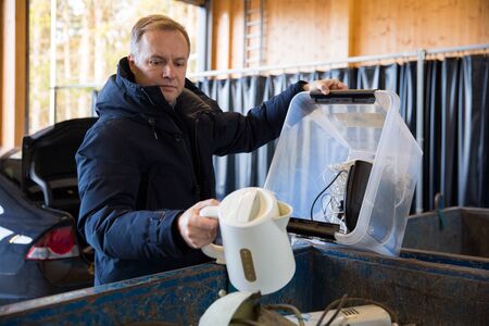 A man putting old appliances into dumpster in sorting centre for safe disposal and recyclingの写真素材