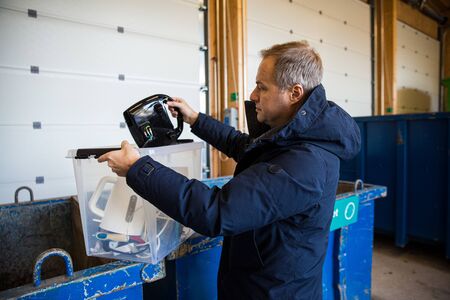 A man putting old appliances into dumpster in sorting centre for safe disposal and recyclingの写真素材